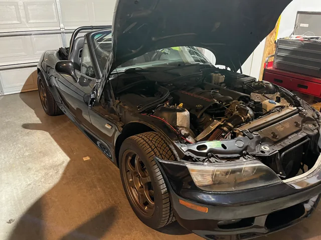 Front-quarter view of the open-top Z3 in the garage, with its hood raised over the LS1 V8 and bronze wheels visible.