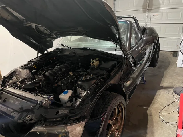 Opposite front-quarter view of the Z3 engine bay, showing the uncovered intake and supporting swap hardware.